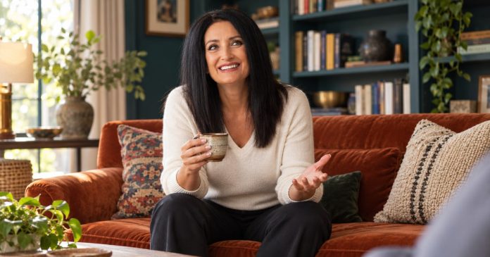 A woman listening and talking with an unseen partner in a comfortable living room.